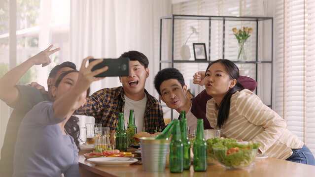Happy hour diner at home relax smile look at camera shooting video photo on mobile app. Group of asia people young adult friend man and woman sit at dining table joy fun talk or eat food drink beer.