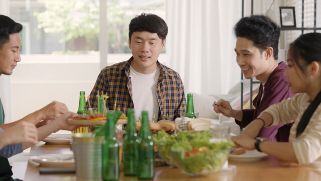 Happy hour good warm summer time diner indoor home. Group of asia people young adult friend man and woman sit at dining table joy fun talk or eat food and drink beer alcohol bottle glass inside house.
