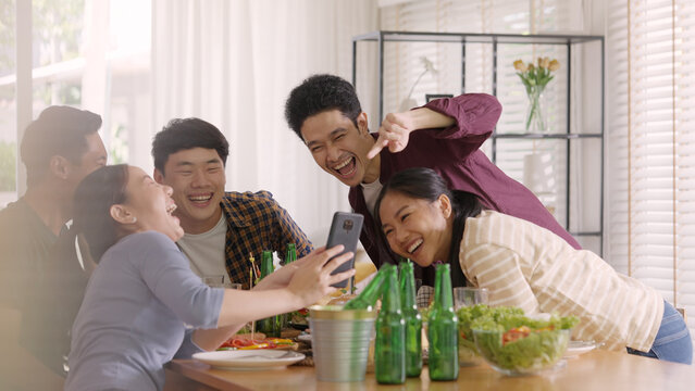 Happy hour diner at home relax smile look at camera shooting video photo on mobile app. Group of asia people young adult friend man and woman sit at dining table joy fun talk or eat food drink beer.
