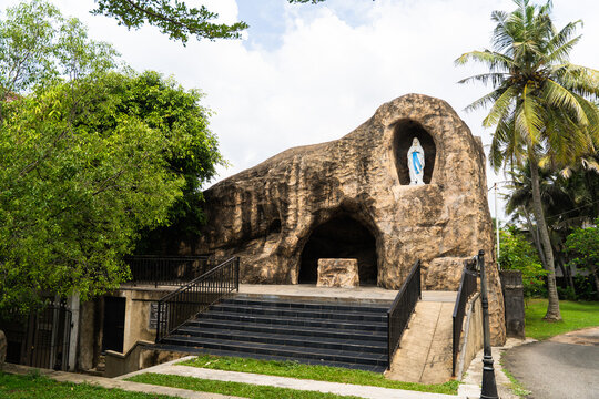 View of a religious grotto with a statue of the Virgin Mary in a rock niche surrounded by lush tropical greenery and palm trees in Galle, Southern Province, Sri Lanka.