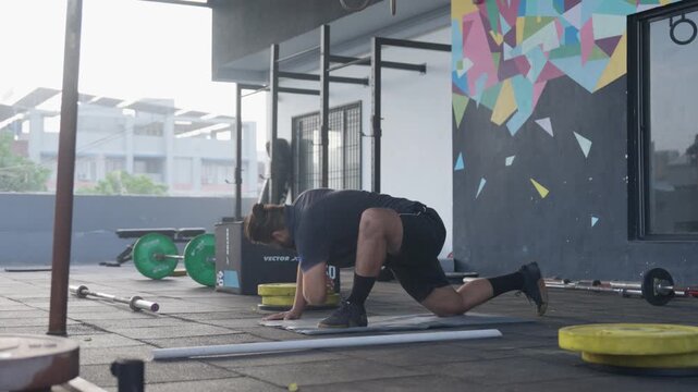 A dedicated Indian bearded athlete performs the world's greatest stretch &mdash; a deep lunge with an overhead arm reach and thoracic rotation &mdash; at a vibrant outdoor CrossFit gym backdrop by a stunning colo