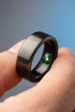 Close up of a person holding a modern black matte smart ring with a glowing green biometric sensor, representing advanced health monitoring and wearable technology innovation.