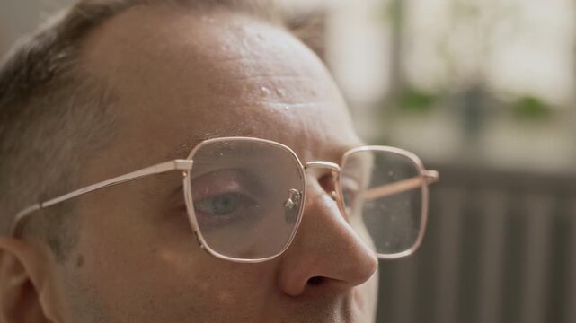 Close up of middle aged Caucasian man sweltering, breathing heavily and wiping sweat from forehead while working in stuffy office