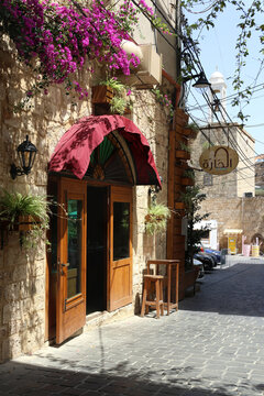 BATROUN, LEBANON  May 18, 2024: Historic street in the town of Batroun featuring a traditional stone building, cobblestone pavement, colorful bougainvillea flowers.