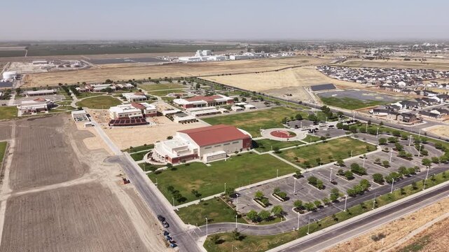 Rotating drone view showing the modern buildings, green lawns, and parking lots of Lemoore College campus, situated in the vast landscape of California's Central Valley on a sunny day