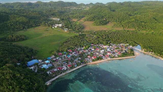 Scenic orbiting aerial view of coastal fishing barangay village amid lush tropical island greenery - Magnesia Del Norte, Catanduanes, Philippines