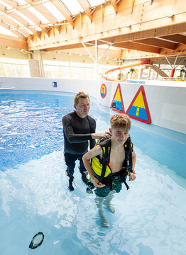 Scuba diving instructor helping a teenage boy adjust his equipment in an indoor swimming pool