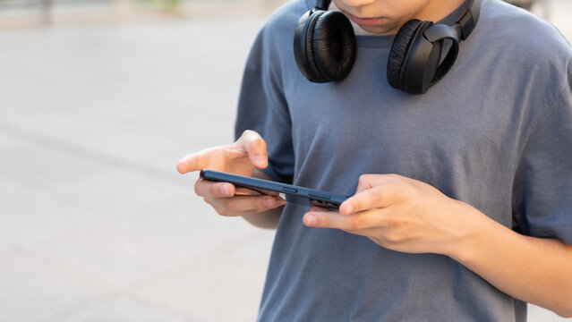 Teenager using smartphone outdoors with headphones around neck, concept of mobile communication, social media and digital lifestyle