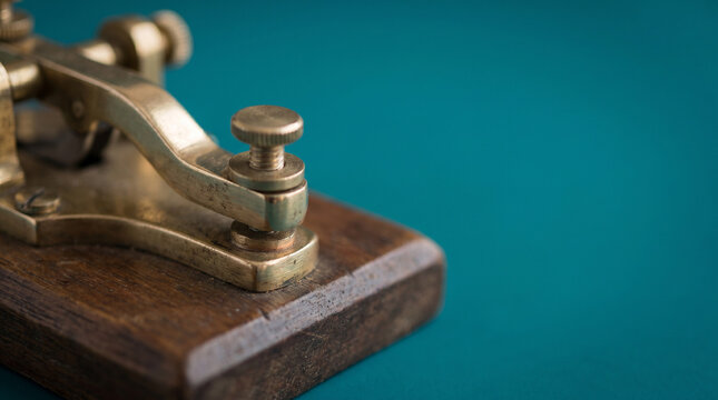 Vintage brass telegraph key with polished lever arm and wooden base on teal background, early data communication and internet precursor concept.