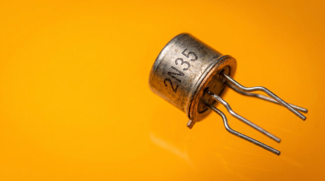 Single vintage germanium transistor with three metal leads splayed from metallic cap on amber background, semiconductor revolution and computing history concept.