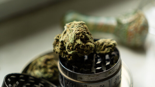 Top down view of a large dry cannabis bud, matches, and an open metal grinder inside a metal stash tin.