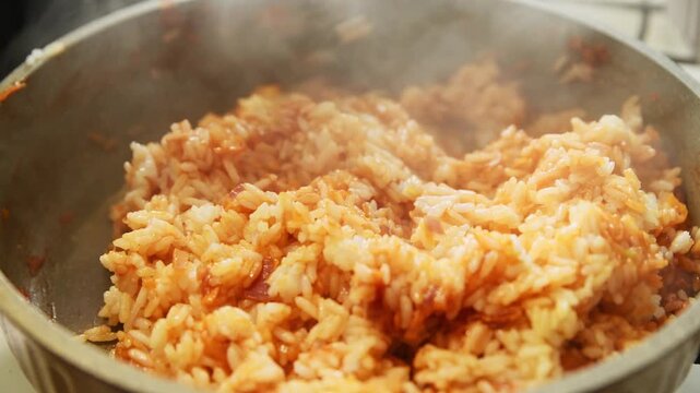 Stirring golden rice with sauteed onion carrot tomato paste in steaming frying pan close-up