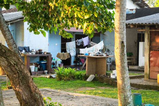 View of a traditional courtyard with laundry hanging on a line and kitchenware on a table under the shade of lush green trees in Galle, Southern Province, Sri Lanka.