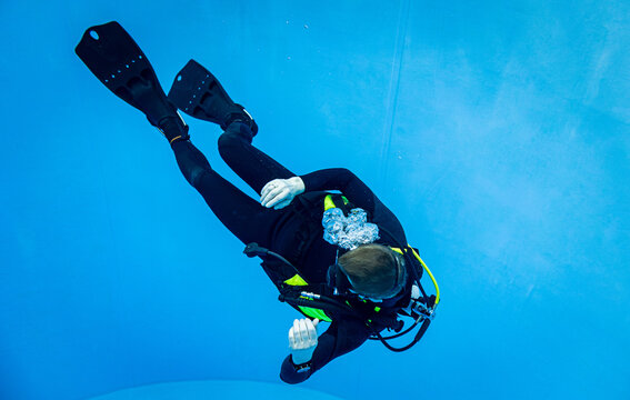 Scuba diver descending in a deep blue swimming pool