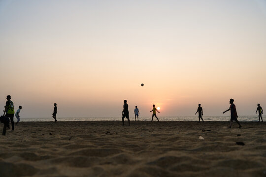 View of silhouetted people playing football on a sandy beach under a warm sunset sky with the ocean in the background Galle, Southern Province, Sri Lanka.