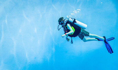 Underwater side view of a young boy scuba diving in a clear blue swimming pool © leszekglasner