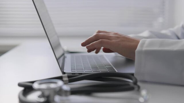 A stethoscope lies on the desk while a physician works on a laptop, emphasizing digital healthcare. The image highlights telehealth, electronic records, and remote medical consultation trends