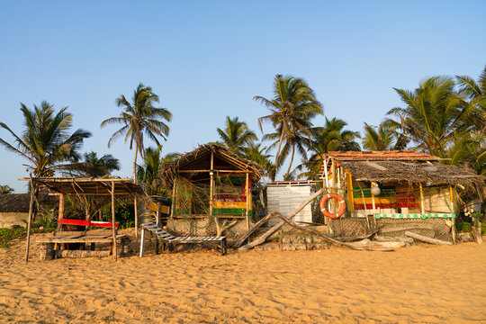 View of rustic beach shacks with thatched roofs and colorful details under palm trees on a sandy shore Galle, Southern Province, Sri Lanka.