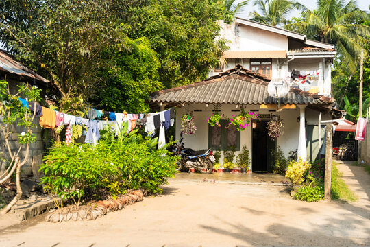 View of a traditional two-story house with a motorcycle parked in front, laundry hanging on a line, and lush tropical greenery in Galle, Southern Province, Sri Lanka.