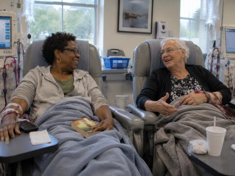Two Elderly Women Laughing During Hemodialysis Treatment in Hospital Dialysis Center