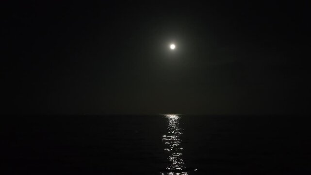 Shining moonlight reflects on water in boundless sea. Full night.
