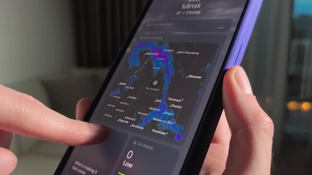 Hands swipe smartphone weather app in a home interior. Forecast maps and temperatures scroll on the screen. Mobile climate checking for daily planning and travel..
