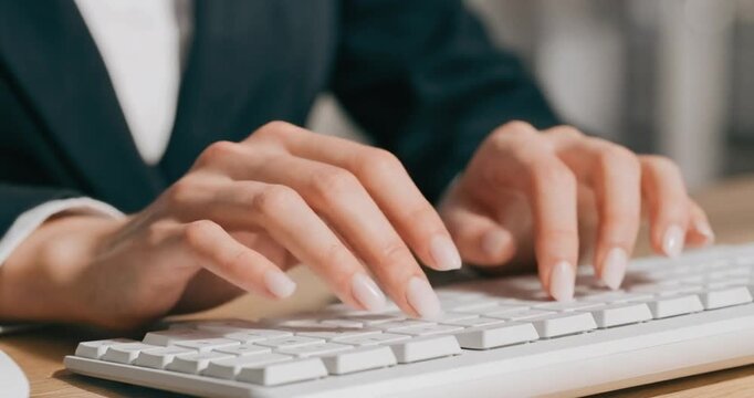 Businesswoman hands typing on white computer keyboard in office workspace setting.