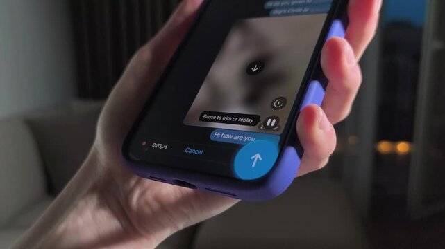Hand holds smartphone in purple case and records a voice message. Thumb taps the chat interface and sending audio Mobile communication, social app use, and device mockup concept..
