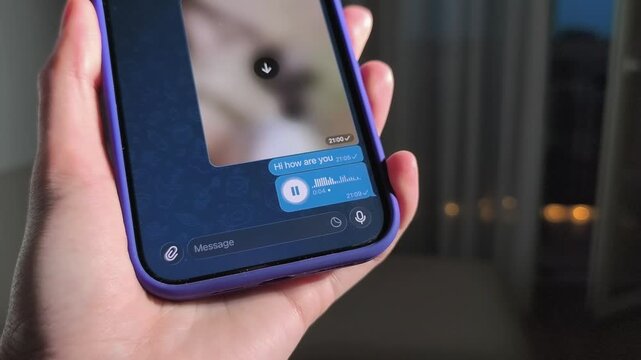 Hand holds smartphone with chat screen and voice message. Thumb taps a mobile messaging interface in close up. Online communication and app mockup concept..