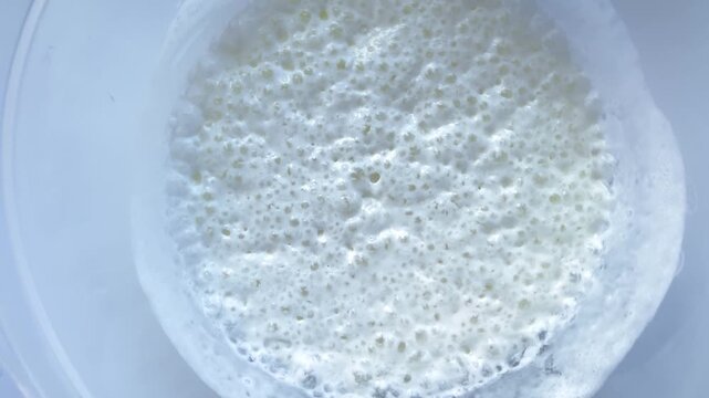 The reaction between baking soda and kefir in bowl, numerous bubbles. Process helps to saturate the mixture with air, making future dough and pastries lighter and more airy when kneading and cooking