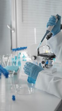 Researcher conducts scientific experiment by carefully pipetting blue solution into flask, surrounded by various laboratory tools. Scene highlights innovation, precision in clinical setting