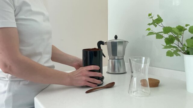 A woman pours freshly ground coffee into an empty glass jar. The morning process of preparing to brew your favorite drink, a habit that helps you tune in to a cheerful and productive morning