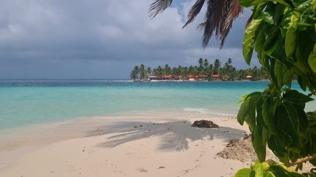 Paradise beach on Isla Perro Chico, San Blas, Panama, with turquoise waves, empty sandy shore, swaying palms, overcast sky and untouched nature, Isla Diablo visible nearby