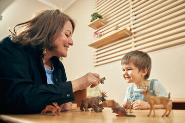 Fototapeta premium Happy boy learning animal names through play with caring preschool educator. Concept of speech development, animal vocabulary, emotional connection, childcare therapy, and early education.