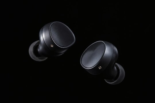 Wireless black earbuds floating on dark background