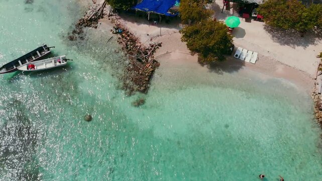 Drone overhead shot of Isla Mucura beach with crystal clear turquoise aquamarine and blue water canoes and sun chairs slowly moving toward island revealing less ocean