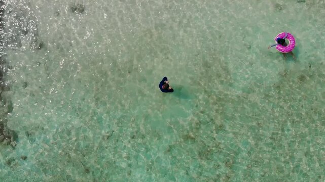 Drone overhead shot of grandfather with mask swimming underwater and granddaughter with donut float in crystal clear Caribbean water at Isla Mucura