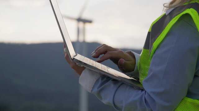A professional in a reflective vest uses a laptop in a wind farm setting, emphasizing clean energy and environmental responsibility. The scene captures modern engineering and eco friendly practices