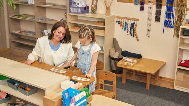 Number matching game in early learning classroom with educator and focused girl. Concept of preschool math, counting skills, childcare education, logic practice, and patient support.