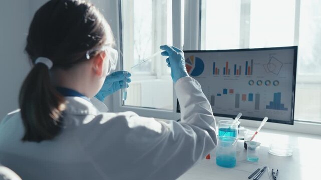 Woman scientist conducts chemical experiments, examines statistical graphs on desktop monitor in bright laboratory. Innovative science, technology drive data driven research, laboratory analysis