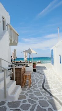 Explore a picturesque coastal path in Naousa, Paros, Greece. Enjoy the stunning views of blue seas and whitewashed buildings while relaxing at charming beachside cafes.