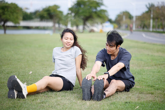 Young Asian Couple Sitting on Grass Stretching Legs After Outdoor Workout
