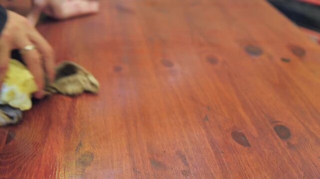 Cleaning a wooden table using a cloth and simple hand motions for a tidy surface in a cozy setting