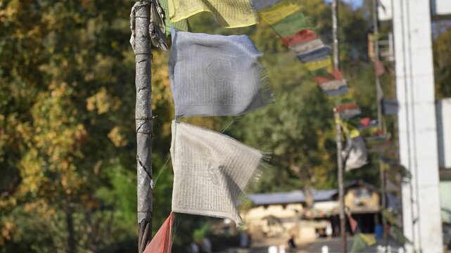 Surkhet, Nepal - 19 May 2026: View of colorful Buddhist prayer flags fluttering in the wind attached to a pole with trees and buildings in the background.