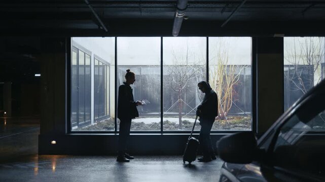 Two shadowy figures meet between parked cars at night, exchanging a suitcase for a thick envelope of money. 