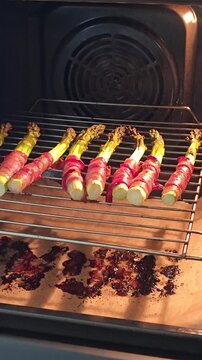 Fresh green asparagus wrapped in bacon roasting on a wire rack inside a hot oven, delicious homemade healthy dinner preparation process close up. Video 4k