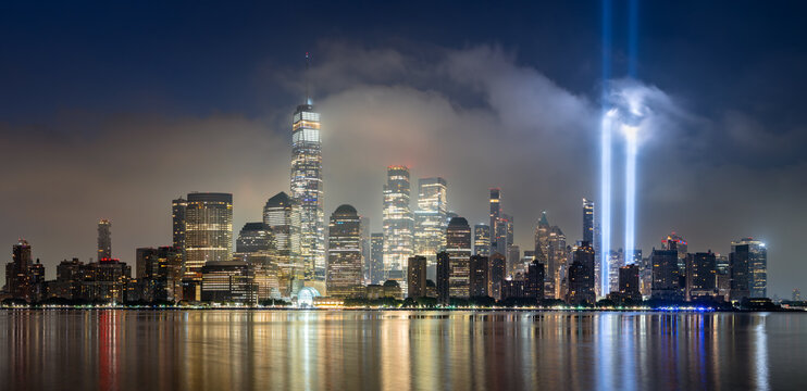 Dawn in Lower Manhattan with skyscrapers and low clouds and the September 11 Tribute in Light memorial lights. Financial District, New York City, USA