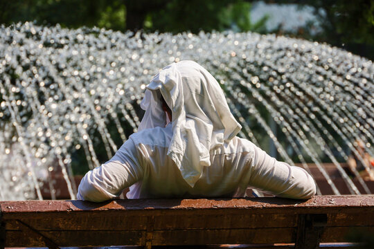 Man with covered head sitting on fountain background in city park. Hot sunny weather