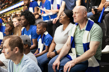 Tense blue team supporters reacting to close call during soccer match in a crowded stadium, wait...