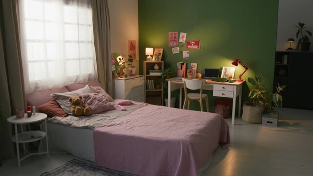 Interior of dimly lit bedroom featuring cozy bed, bedside table with pill bottles, laptop and red lamp on wooden desk against green wall decorated with posters